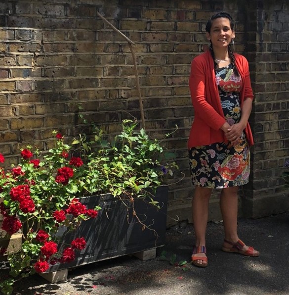 Eurydice ‘Eury’ Caldwell, founder of GENER8TE, standing by flowers in a red cardigan